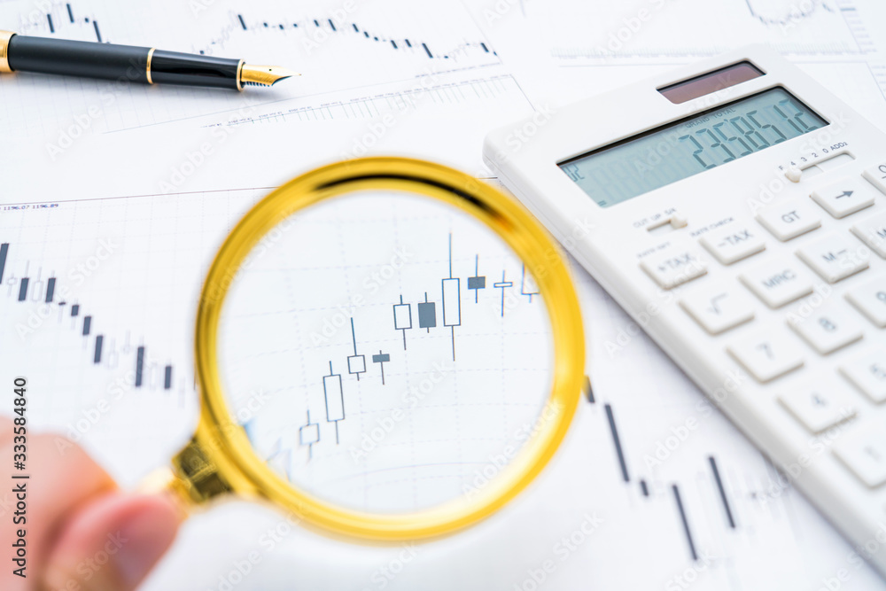 Calculator, magnifying glass, coins and pen on a bar chart-stock finance concept image Calculator, magnifying glass, coins and pen on a bar chart-stock finance concept image
