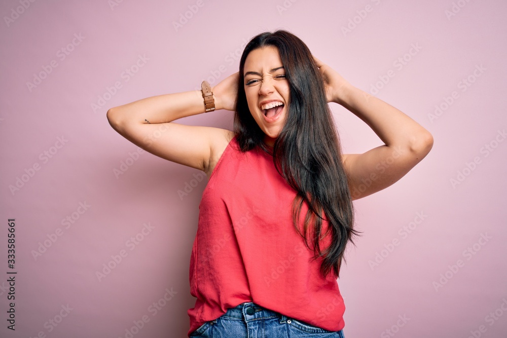 Young brunette woman wearing casual summer shirt over pink isolated background relaxing and stretching, arms and hands behind head and neck smiling happy Young brunette woman wearing casual summer shirt over pink isolated background relaxing and stretching, arms and hands behind head and neck smiling happy