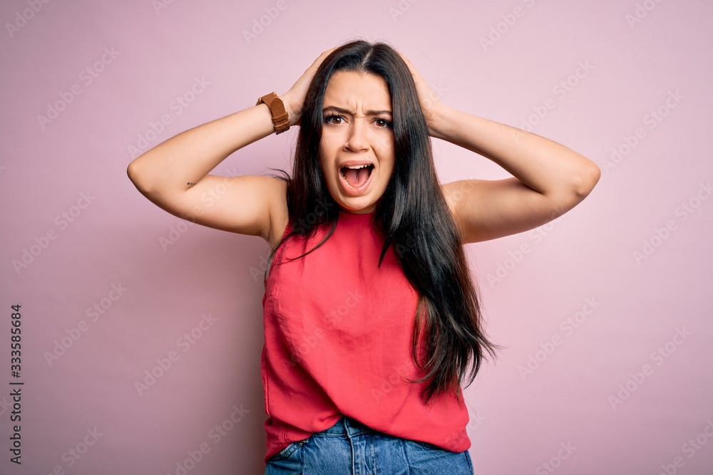 Young brunette woman wearing casual summer shirt over pink isolated background Crazy and scared with hands on head, afraid and surprised of shock with open mouth