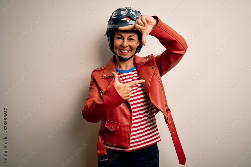 Middle age motorcyclist woman wearing motorcycle helmet and jacket over white background smiling making frame with hands and fingers with happy face. Creativity and photography concept. Middle age motorcyclist woman wearing motorcycle helmet and jacket over white background smiling making frame with hands and fingers with happy face. Creativity and photography concept.