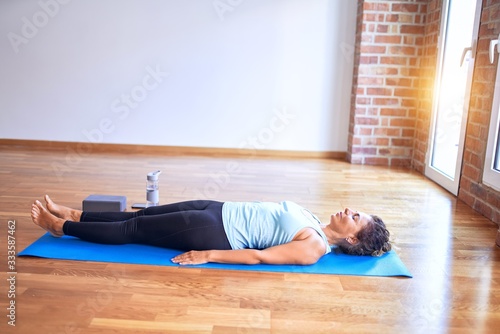 Middle age beautiful sportwoman lying down on mat practicing yoga doing corpose pose at gym photo