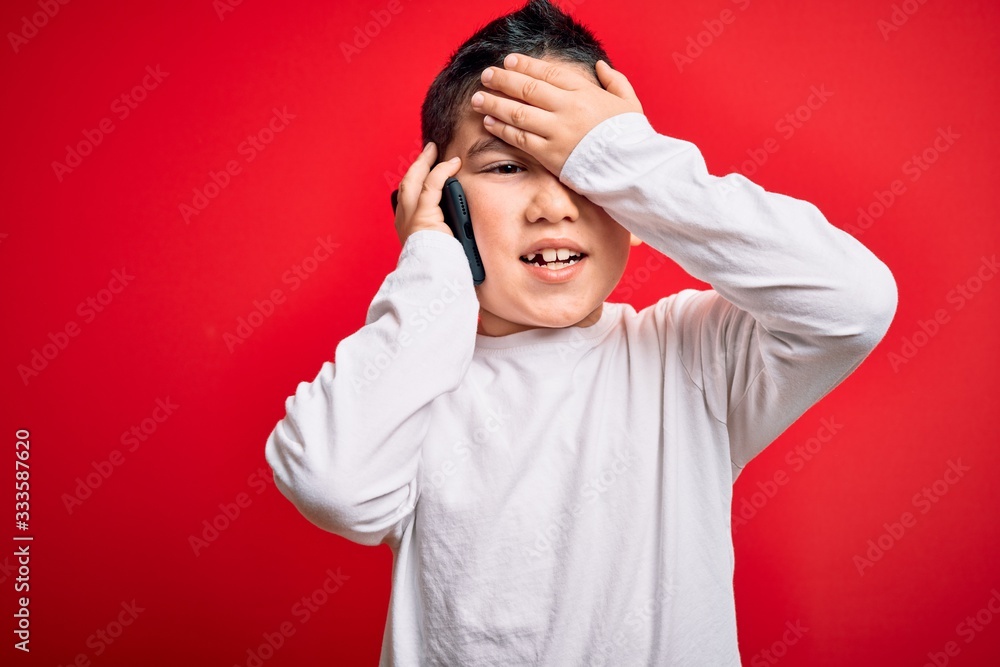 Young little boy kid talking on smartphone mobile over red isolated background stressed with hand on head, shocked with shame and surprise face, angry and frustrated. Fear and upset for mistake. Young little boy kid talking on smartphone mobile over red isolated background stressed with hand on head, shocked with shame and surprise face, angry and frustrated. Fear and upset for mistake.