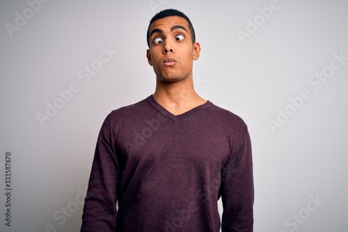 Young handsome african american man wearing casual sweater over white background making fish face with lips, crazy and comical gesture. Funny expression.