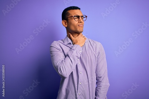 Handsome african american man wearing striped shirt and glasses over purple background Touching painful neck, sore throat for flu, clod and infection © Krakenimages.com