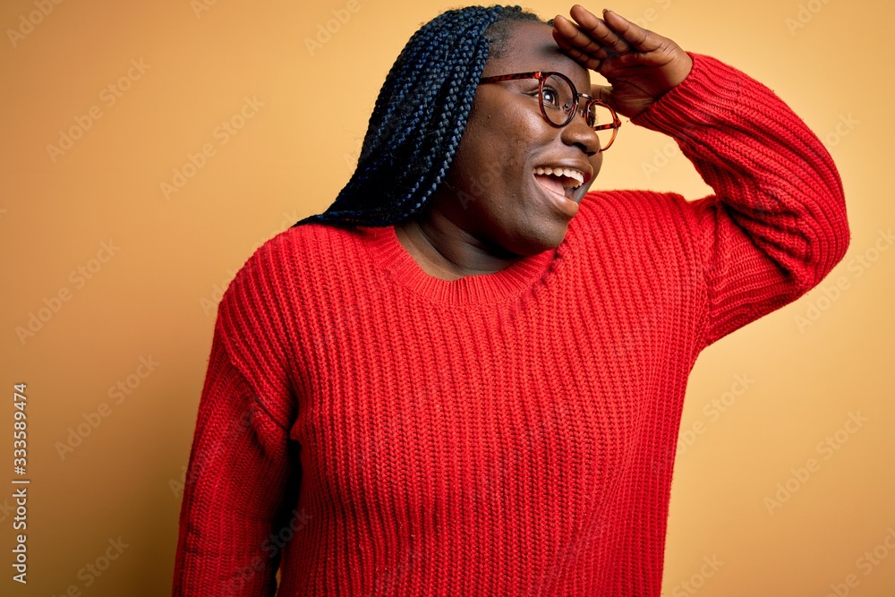 African american plus size woman with braids wearing casual sweater over yellow background very happy and smiling looking far away with hand over head. Searching concept. African american plus size woman with braids wearing casual sweater over yellow background very happy and smiling looking far away with hand over head. Searching concept.