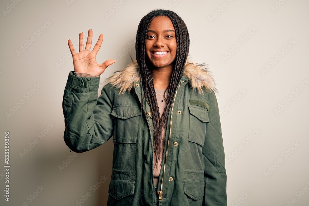 Young african american woman wearing winter parka coat over isolated background showing and pointing up with fingers number five while smiling confident and happy. Young african american woman wearing winter parka coat over isolated background showing and pointing up with fingers number five while smiling confident and happy.