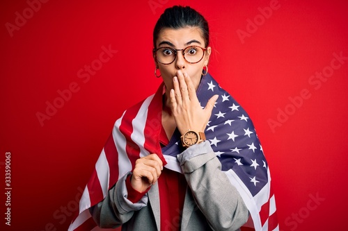 Young beautiful brunette patriotic woman wearing usa flag celebrating independence day cover mouth with hand shocked with shame for mistake, expression of fear, scared in silence, secret concept