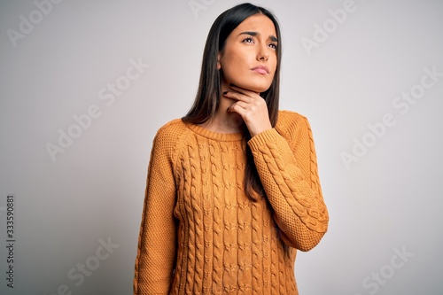Young beautiful brunette woman wearing casual sweater over isolated white background Touching painful neck, sore throat for flu, clod and infection