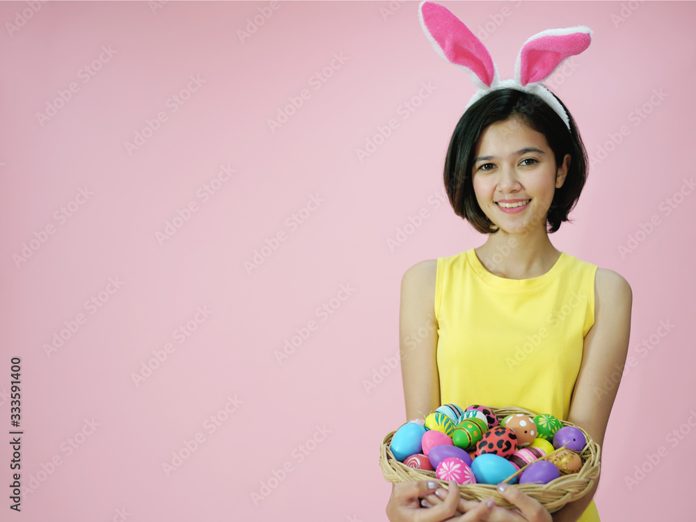 Cute girl with bunny ears and basket full of Easter eggs on pink background with copy space Cute girl with bunny ears and basket full of Easter eggs on pink background with copy space