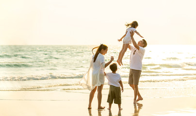 Happy Young Asian happy family parents with child walking and having fun together on the beach at sunset in summertime. Father, mother and kids relax and enjoy summer lifestyle travel holiday vacation