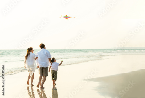 Happy Young Asian family parents with child running and having fun with playing kite together on the beach in summertime. Father, mother and kids relax and enjoy summer lifestyle travel vacation