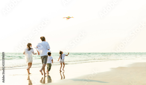 Happy Young Asian family parents with child running and having fun with playing kite together on the beach in summertime. Father, mother and kids relax and enjoy summer lifestyle travel vacation