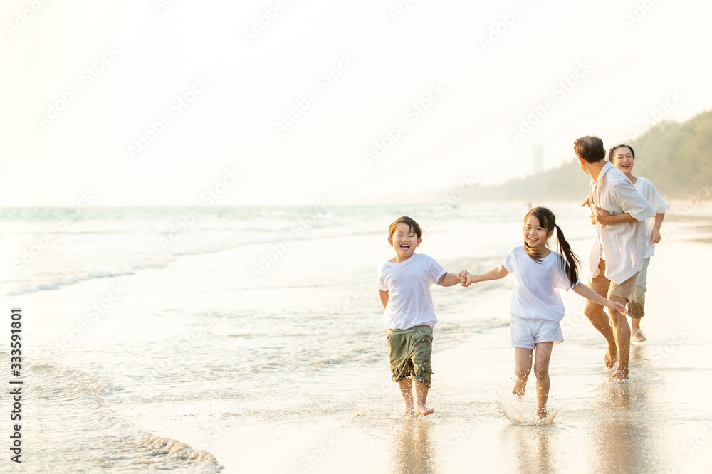Happy Asian family grandparents with grandchild running and having fun together on the beach in summertime. Grandpa and grandma with kids relax and enjoy summer lifestyle travel holiday vacation.