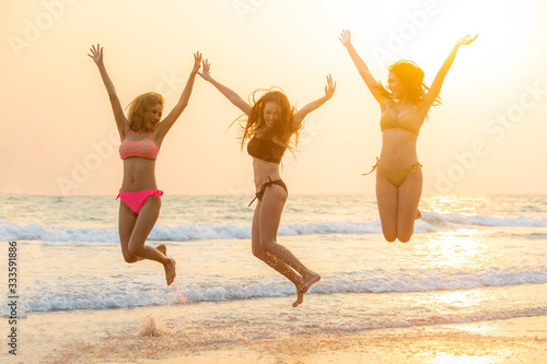 Group of Happy young beautiful Asian women in bikini swimwear playing and jumping together on the beach at sunset. Three sexy girls friends relax and having fun in summer holidays vacation travel