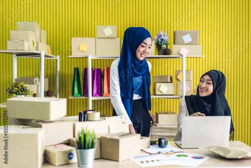 Portrait of smiling beautiful two muslim owner asian woman freelancer sme business online shopping working on laptop computer with parcel box on table at home - Business online shipping and delivery photo