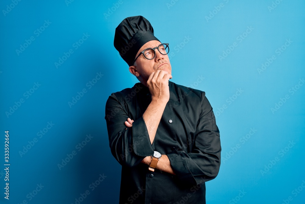 Middle age handsome grey-haired chef man wearing cooker uniform and hat with hand on chin thinking about question, pensive expression. Smiling with thoughtful face. Doubt concept. Middle age handsome grey-haired chef man wearing cooker uniform and hat with hand on chin thinking about question, pensive expression. Smiling with thoughtful face. Doubt concept.