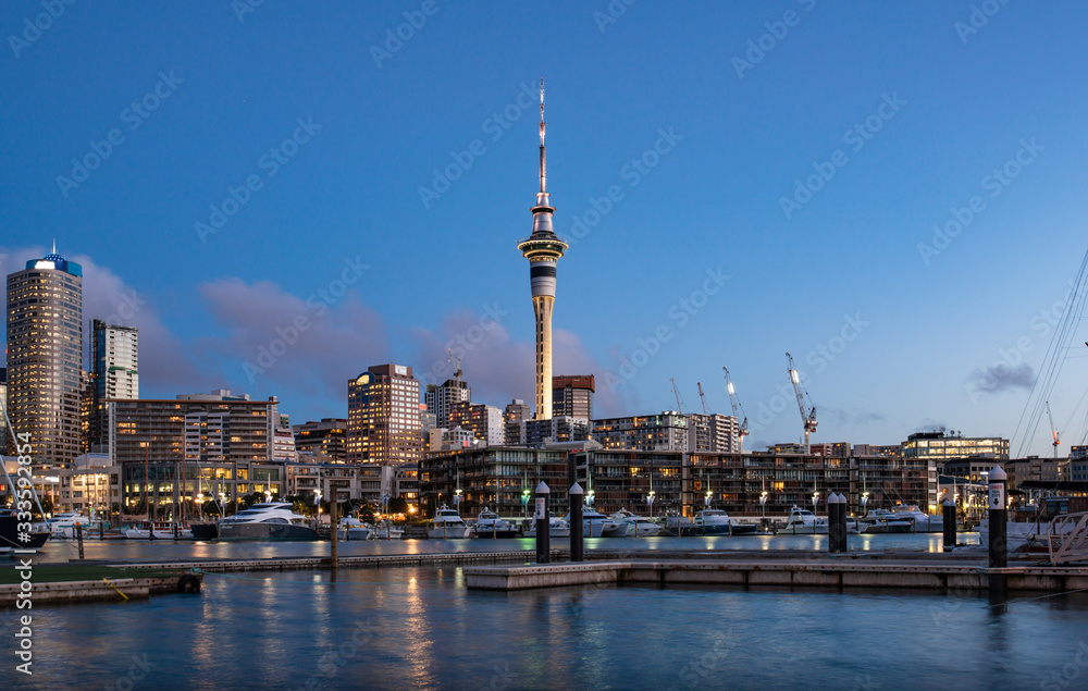 Twilight view of sky tower view from Viaduct Harbour in the central of Auckland, New Zealand. Auckland is New Zealand's largest city and the centre of the country's retail and commercial activities. - obrazy, fototapety, plakaty 