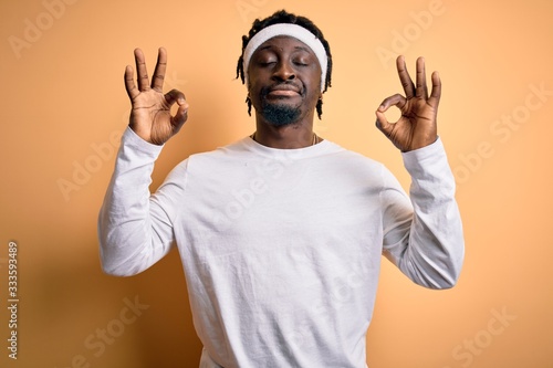 Young african american man doing sport wearing sportswer over isolated yellow background relax and smiling with eyes closed doing meditation gesture with fingers. Yoga concept.