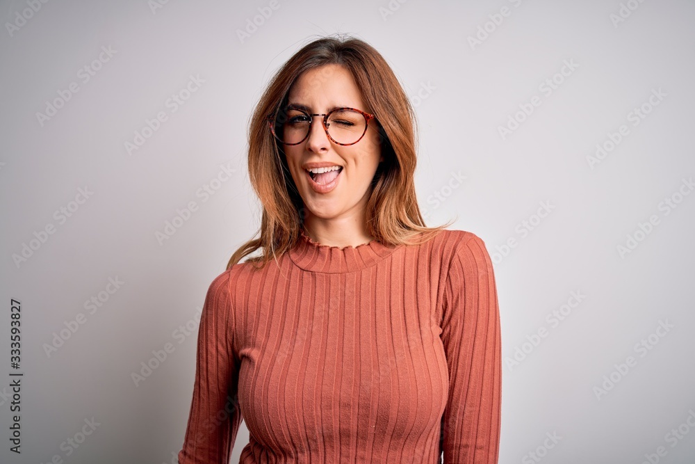 Obraz premium Young beautiful brunette woman wearing casual sweater and glasses over white background winking looking at the camera with sexy expression, cheerful and happy face.