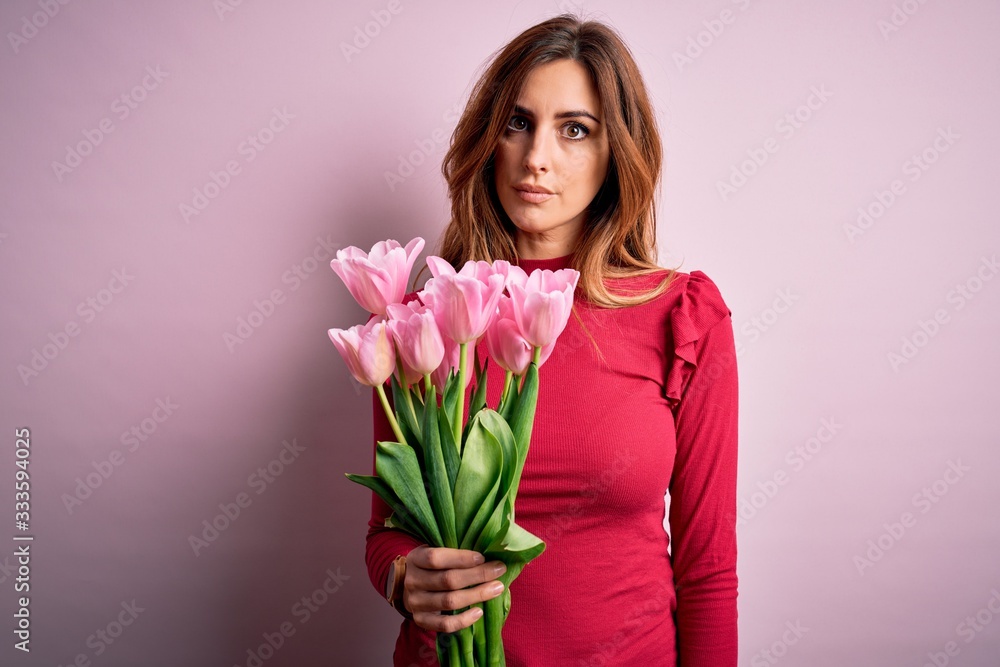 Young beautiful brunette woman holding bouquet of pink tulips over isolated background Relaxed with serious expression on face. Simple and natural looking at the camera. Young beautiful brunette woman holding bouquet of pink tulips over isolated background Relaxed with serious expression on face. Simple and natural looking at the camera.