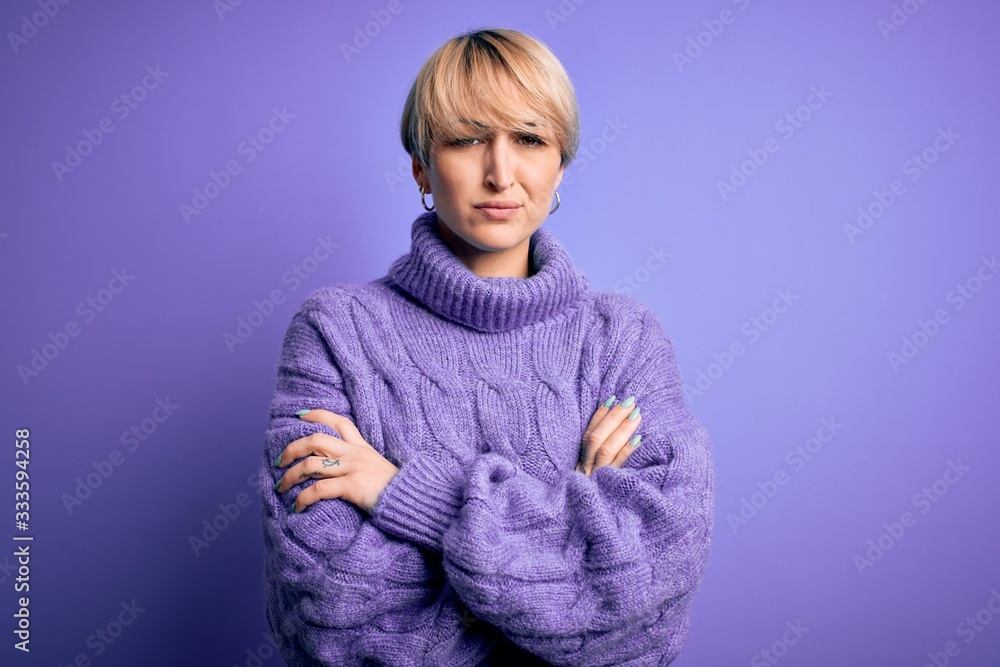 Young blonde woman with short hair wearing winter turtleneck sweater over purple background skeptic and nervous, disapproving expression on face with crossed arms. Negative person. Young blonde woman with short hair wearing winter turtleneck sweater over purple background skeptic and nervous, disapproving expression on face with crossed arms. Negative person.