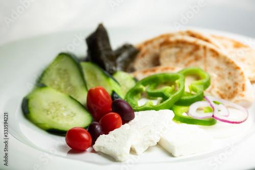 Shallow focus view of simple Greek meze food platter; with vegetables, pita, feta, and grape leaves