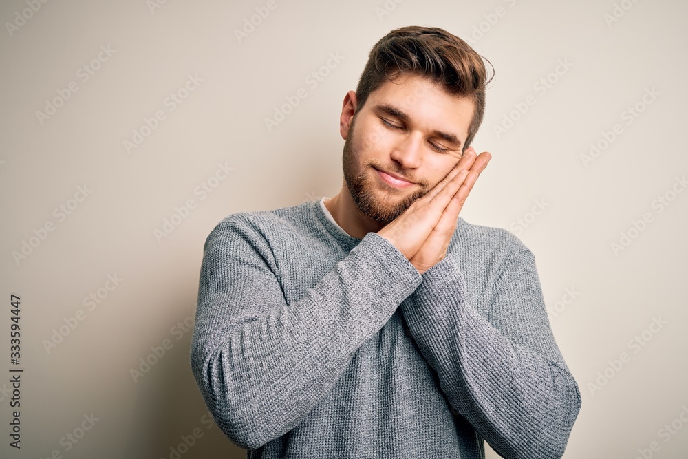 Young handsome blond man with beard and blue eyes wearing casual sweater sleeping tired dreaming and posing with hands together while smiling with closed eyes. Young handsome blond man with beard and blue eyes wearing casual sweater sleeping tired dreaming and posing with hands together while smiling with closed eyes.