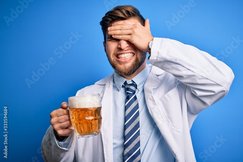 Young blond doctor man with beard and blue eyes wearing coat drinking jar of beer stressed with hand on head, shocked with shame and surprise face, angry and frustrated. Fear and upset for mistake.
