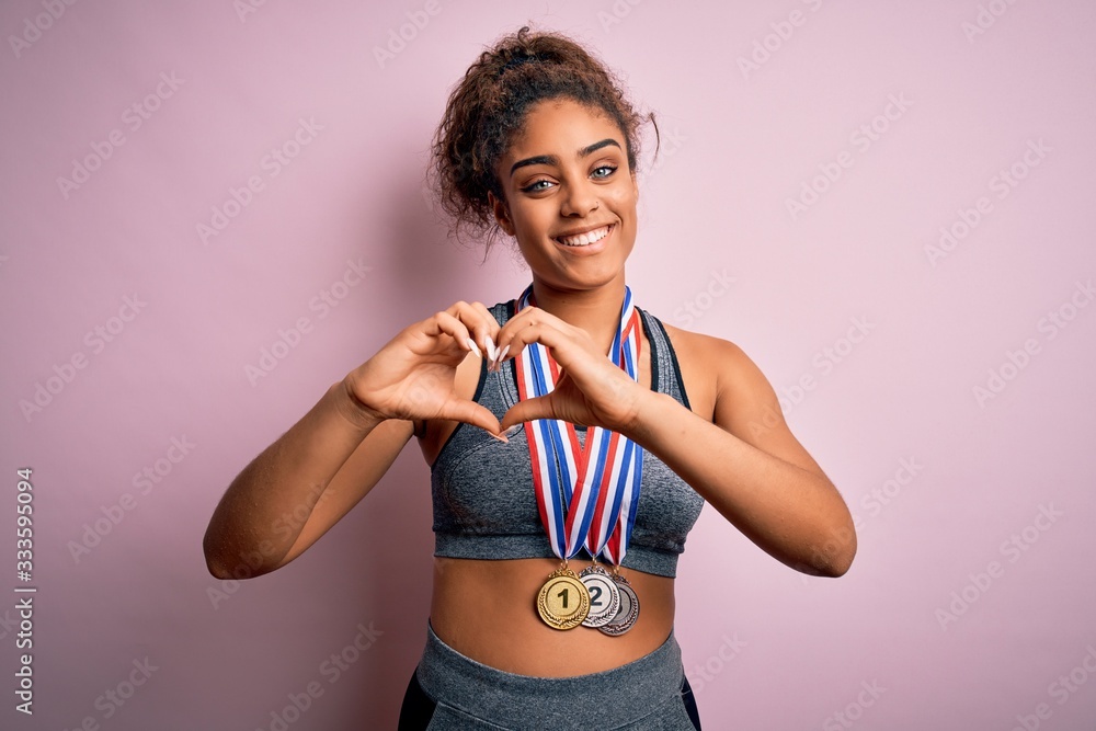 Young african american sporty girl doing sport winning medals over isolated pink background smiling in love showing heart symbol and shape with hands. Romantic concept.