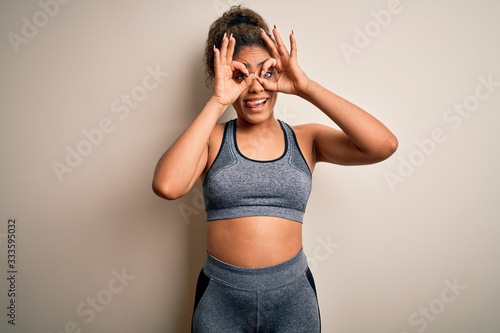 Young african american sportswoman doing sport wearing sportswear over white background doing ok gesture like binoculars sticking tongue out, eyes looking through fingers. Crazy expression.