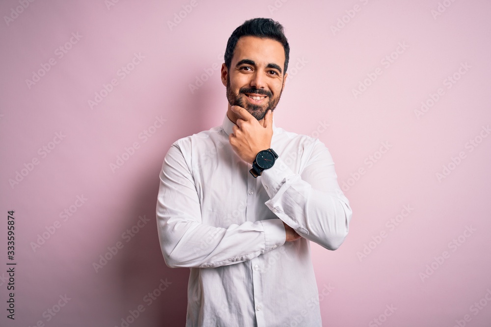Young handsome man with beard wearing casual shirt standing over pink background looking confident at the camera smiling with crossed arms and hand raised on chin. Thinking positive. Young handsome man with beard wearing casual shirt standing over pink background looking confident at the camera smiling with crossed arms and hand raised on chin. Thinking positive.