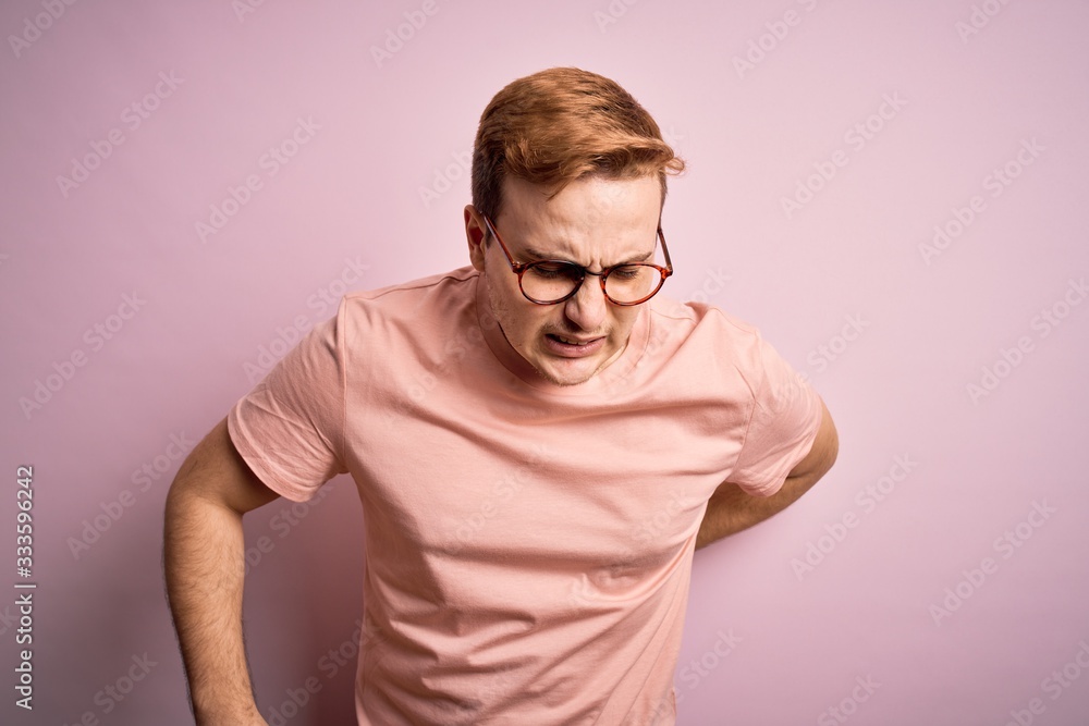 Young handsome redhead man wearing casual t-shirt standing over isolated pink background Suffering of backache, touching back with hand, muscular pain Young handsome redhead man wearing casual t-shirt standing over isolated pink background Suffering of backache, touching back with hand, muscular pain