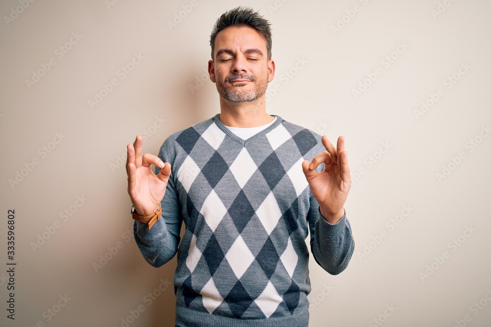 Young handsome man wearing casual sweater standing over isolated white background relax and smiling with eyes closed doing meditation gesture with fingers. Yoga concept. Young handsome man wearing casual sweater standing over isolated white background relax and smiling with eyes closed doing meditation gesture with fingers. Yoga concept.