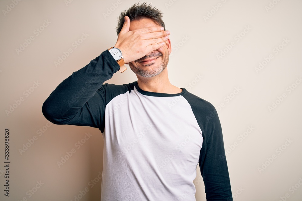 Young handsome man wearing casual t-shirt standing over isolated white background smiling and laughing with hand on face covering eyes for surprise. Blind concept. Young handsome man wearing casual t-shirt standing over isolated white background smiling and laughing with hand on face covering eyes for surprise. Blind concept.