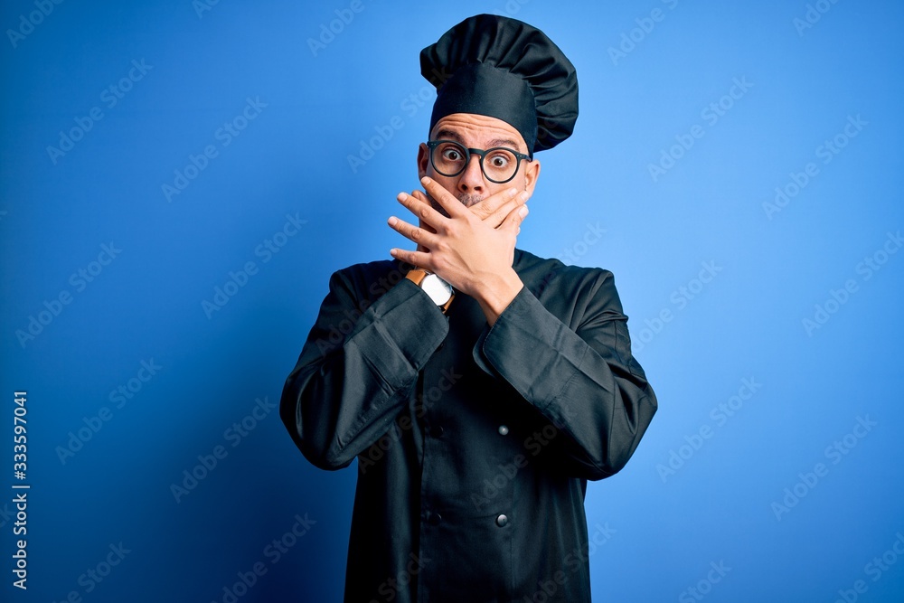 Young handsome chef man wearing cooker uniform and hat over isolated blue background shocked covering mouth with hands for mistake. Secret concept. Young handsome chef man wearing cooker uniform and hat over isolated blue background shocked covering mouth with hands for mistake. Secret concept.