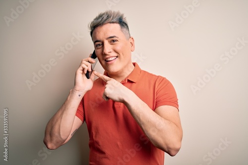 Young modern man having a conversation talking on smartphone over isolated background very happy pointing with hand and finger © Krakenimages.com