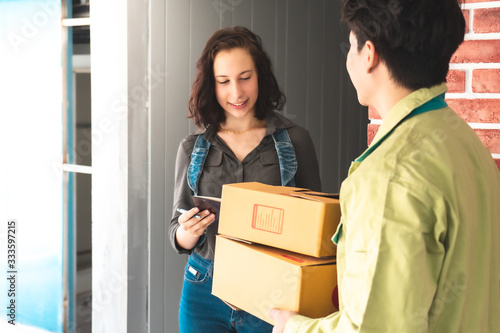 Fotografi Asian delivery man holding a cardboard box while waiting beautiful woman putting signature for confirm receive