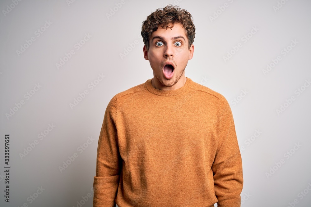 Young blond handsome man with curly hair wearing casual sweater over white background afraid and shocked with surprise and amazed expression, fear and excited face. Young blond handsome man with curly hair wearing casual sweater over white background afraid and shocked with surprise and amazed expression, fear and excited face.