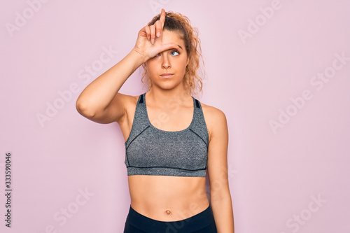 Young beautiful blonde sportswoman with blue eyes doing exercise wearing sportswear making fun of people with fingers on forehead doing loser gesture mocking and insulting.