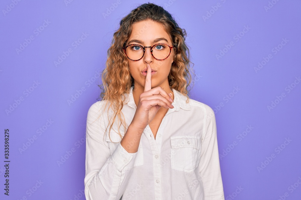 Young beautiful woman with blue eyes wearing casual shirt and glasses over purple background asking to be quiet with finger on lips. Silence and secret concept. Young beautiful woman with blue eyes wearing casual shirt and glasses over purple background asking to be quiet with finger on lips. Silence and secret concept.