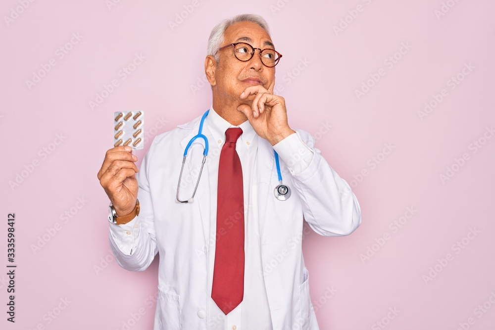 Middle age senior grey-haired doctor man holding prescription pills over pink background serious face thinking about question, very confused idea Middle age senior grey-haired doctor man holding prescription pills over pink background serious face thinking about question, very confused idea