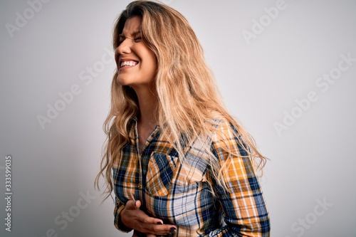 Young beautiful blonde woman wearing casual shirt standing over isolated white background with hand on stomach because nausea, painful disease feeling unwell. Ache concept.