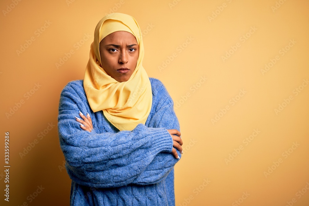 Young African American afro woman wearing muslim hijab over isolated yellow background skeptic and nervous, disapproving expression on face with crossed arms. Negative person. Young African American afro woman wearing muslim hijab over isolated yellow background skeptic and nervous, disapproving expression on face with crossed arms. Negative person.