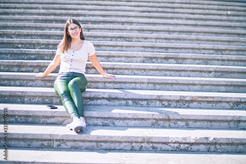Young beautiful woman smiling happy and confident. Sitting on stairs with smile on face at the town street