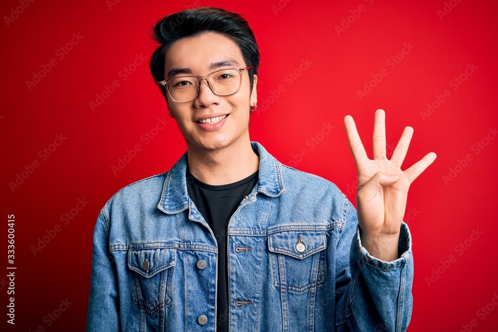 Young handsome chinese man wearing denim jacket and glasses over red background showing and pointing up with fingers number four while smiling confident and happy. Young handsome chinese man wearing denim jacket and glasses over red background showing and pointing up with fingers number four while smiling confident and happy.
