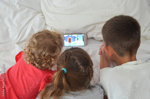 group caucasian children rear view lie on the bed and watch cartoons on their cell phone