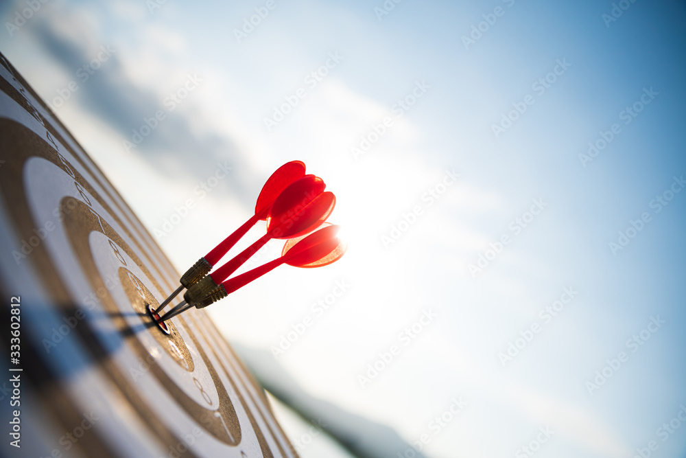 © Siam - Close up shot red darts arrows in the target center on dark blue sky background. Business target or goal success and winner concept.