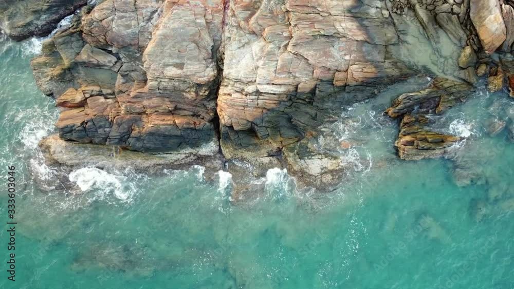 Aerial top view of beautiful tropical island rocky seashore with clear turquoise green ocean waves with white foam splashing and crashing the rocky cliff at sunset. Beauty of nature in summer concept. Aerial top view of beautiful tropical island rocky seashore with clear turquoise green ocean waves with white foam splashing and crashing the rocky cliff at sunset. Beauty of nature in summer concept.
