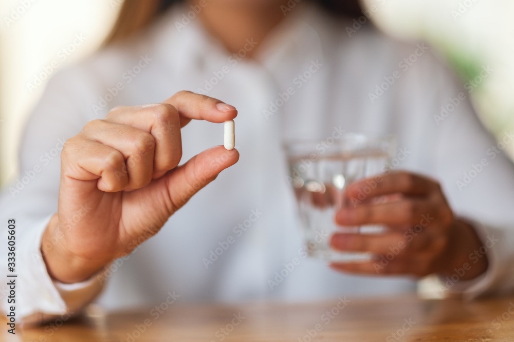 Closeup image of a woman holding a white pill and a glass of water Closeup image of a woman holding a white pill and a glass of water