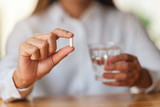 Closeup image of a woman holding a white pill and a glass of water